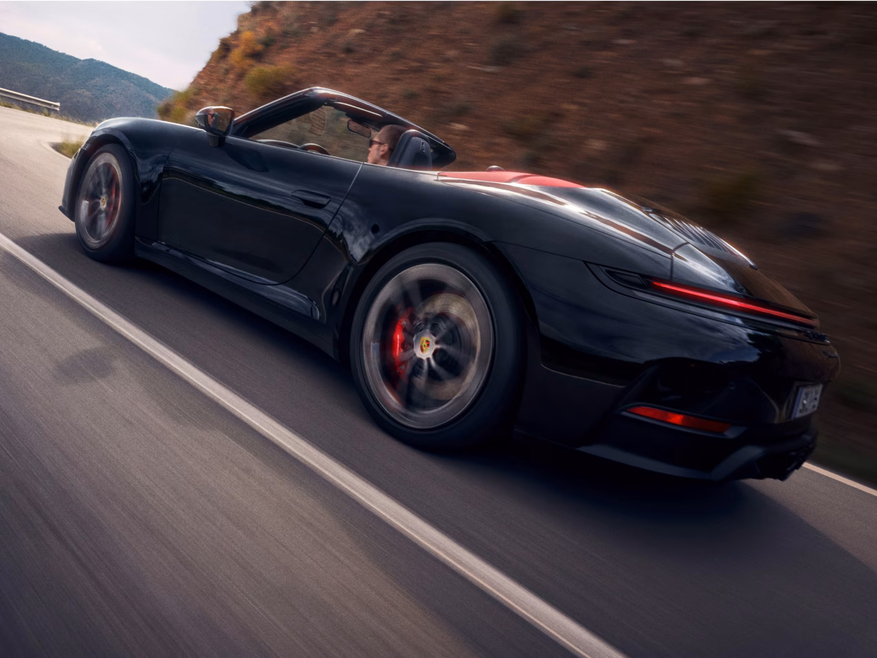 Porsche 911 Carrera GTS Cabriolet in Schwarz fährt auf Straße durch bergige Landschaft. Blick auf die Seite.