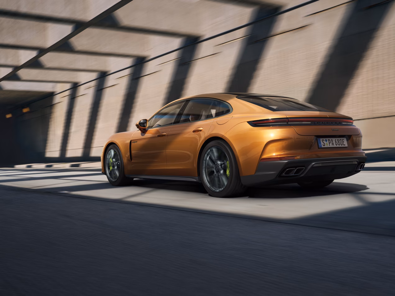 Porsche Panamera Turbo E-Hybrid in Madeira Gold Metallic driving on a street. Rear and side view from behind.