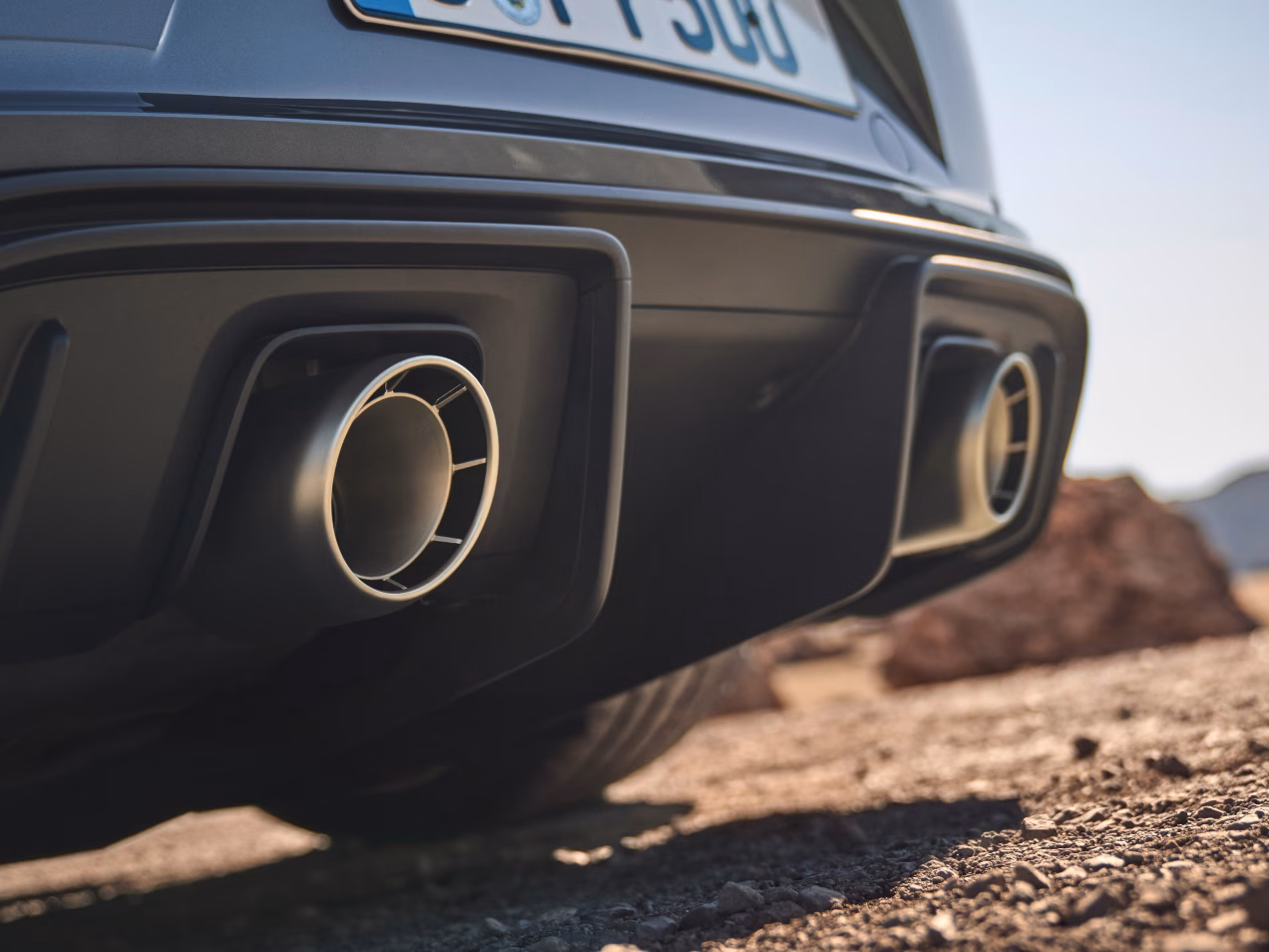 Porsche 718 Spyder RS in Vanadium Grey Metallic driving along a street. Bottom view of rear end and side.