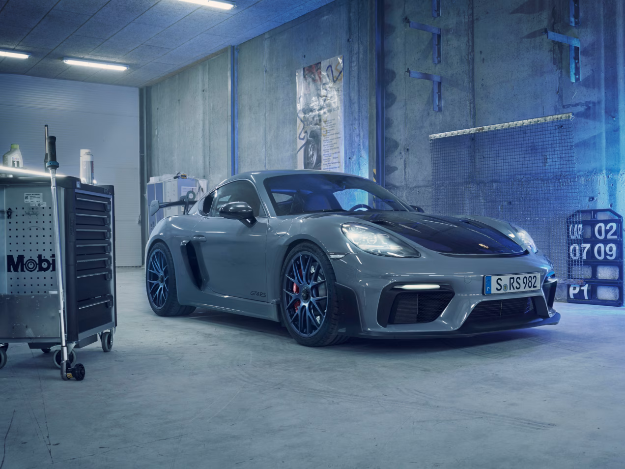 Porsche 718 Cayman GT4 RS in Arktikgrau mit Weissach-Paket steht in Garage. Blick auf Front und Seite.