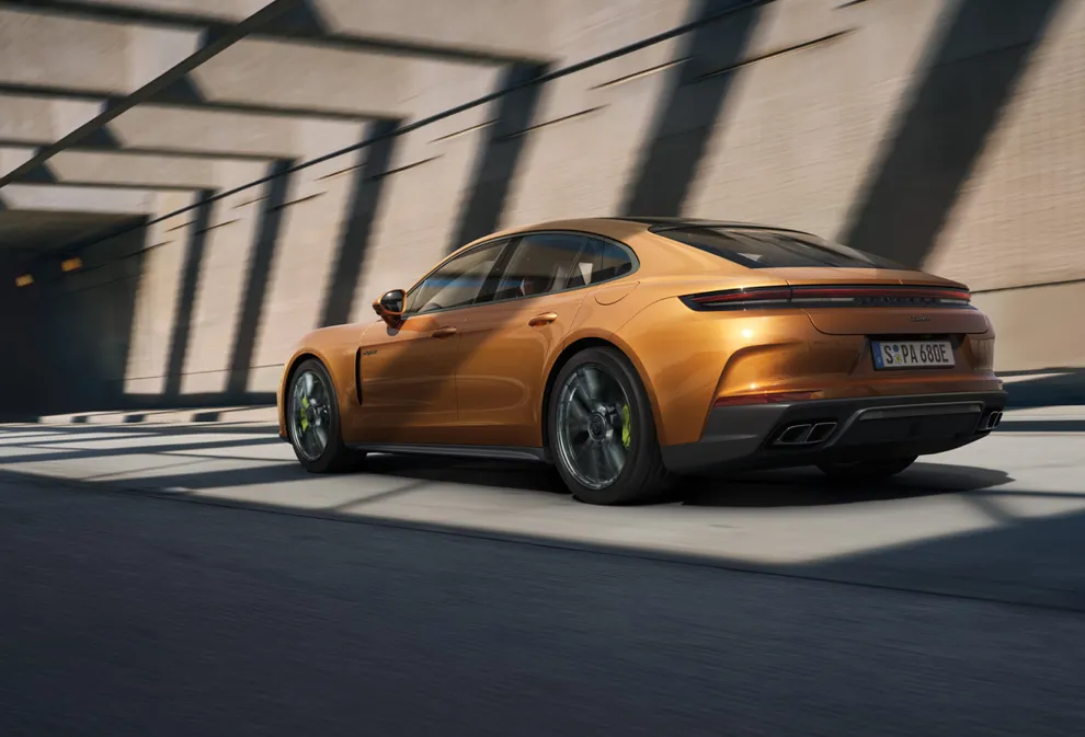 Porsche Panamera Turbo E-Hybrid in Madeira Gold Metallic driving on a street. Rear and side view from behind.