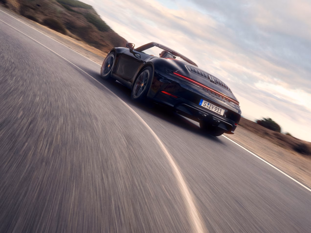 Porsche 911 Carrera GTS Cabriolet in Black driving through a corner on a road. View of rear end from behind.