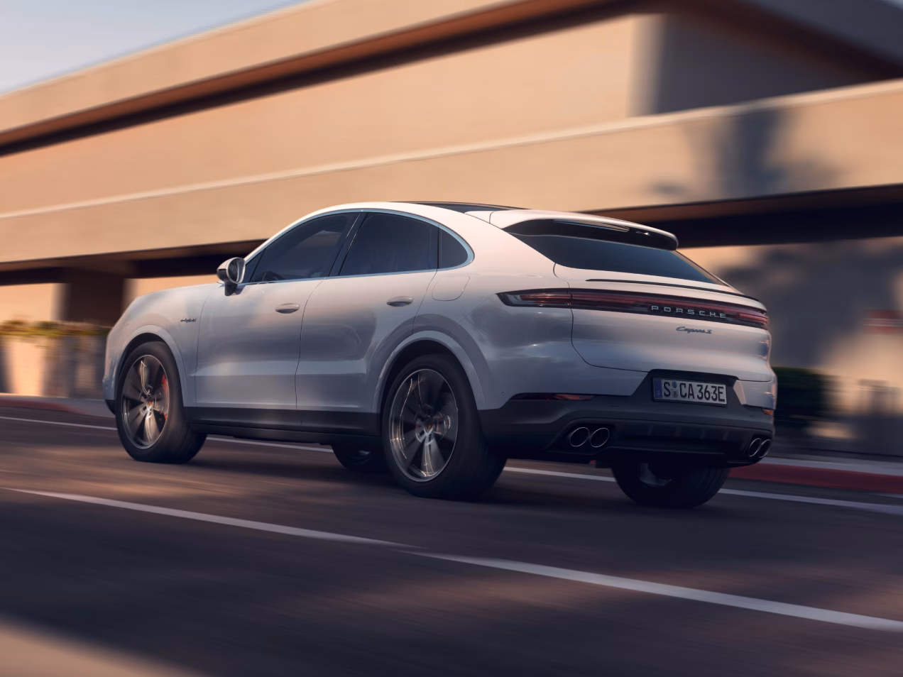 Porsche Cayenne S E-Hybrid Coupé in Carrara White Metallic driving along a highway. Rear and side view from behind.