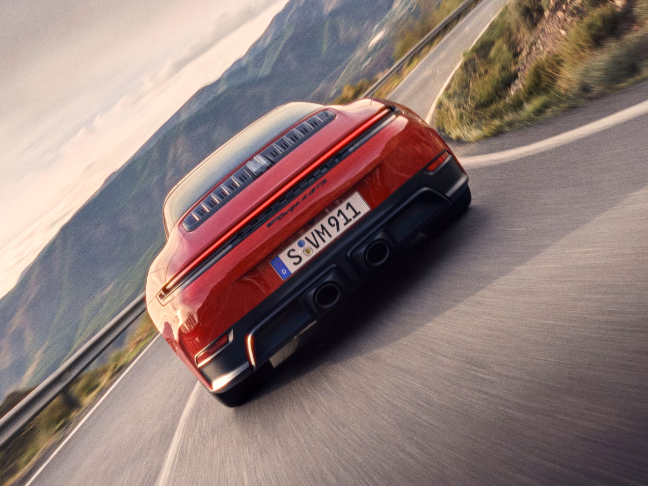 Porsche 911 Targa 4 GTS in Carmine Red driving on a road. View of rear end from behind.