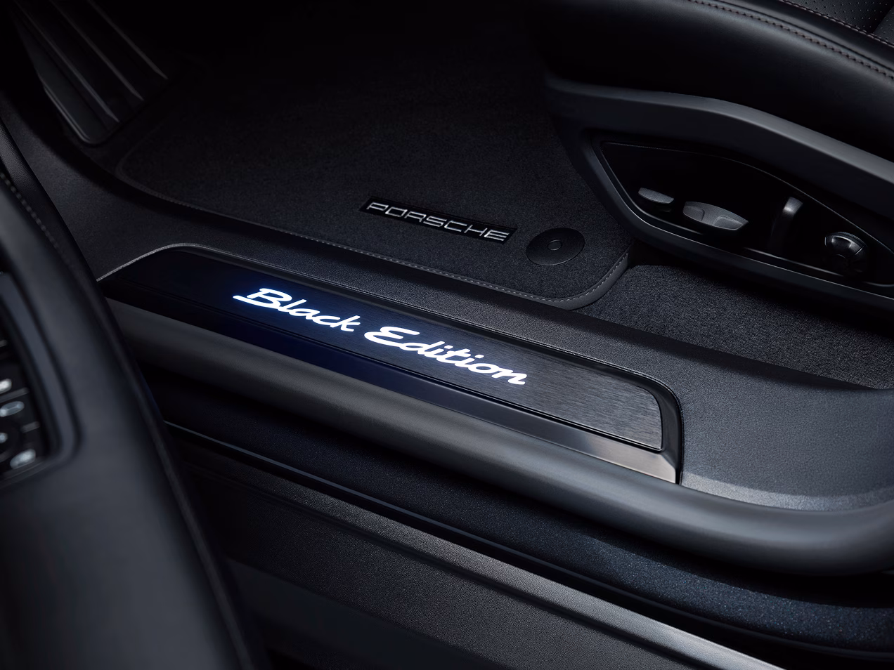 Detailansicht der Türeinstiegsblenden aus gebürstetem schwarzem Aluminium mit weiß beleuchtetem Modellschriftzug beim Porsche Taycan 4S Black Edition mit Erweiterungspaket Black Edition.