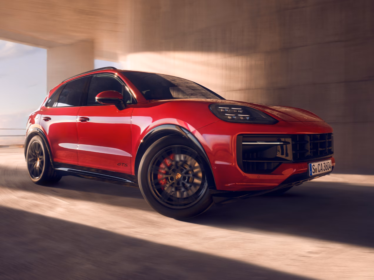 Zicht van voren op de voorkant van een optrekkende Porsche Cayenne GTS in karmijnrood.