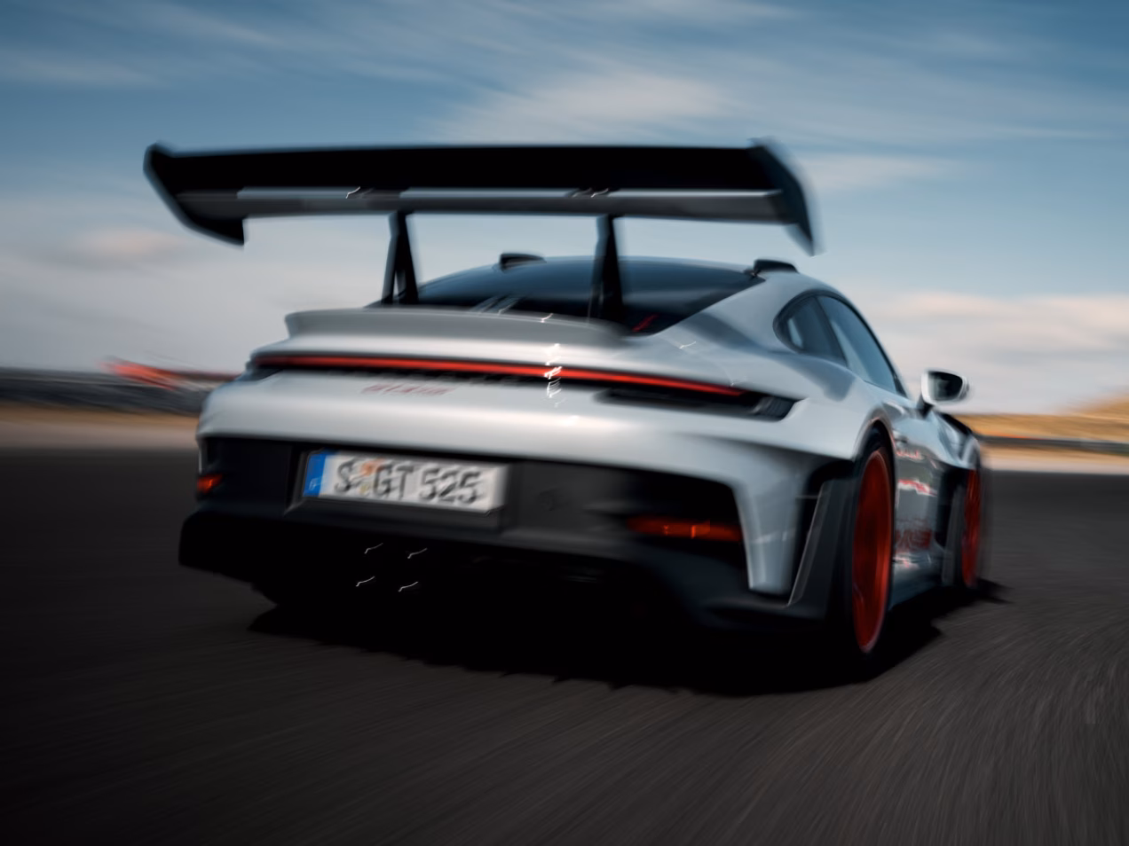 The Porsche 911 GT3 RS in Ice Grey Metallic driving on a rack track. View of rear end from behind.