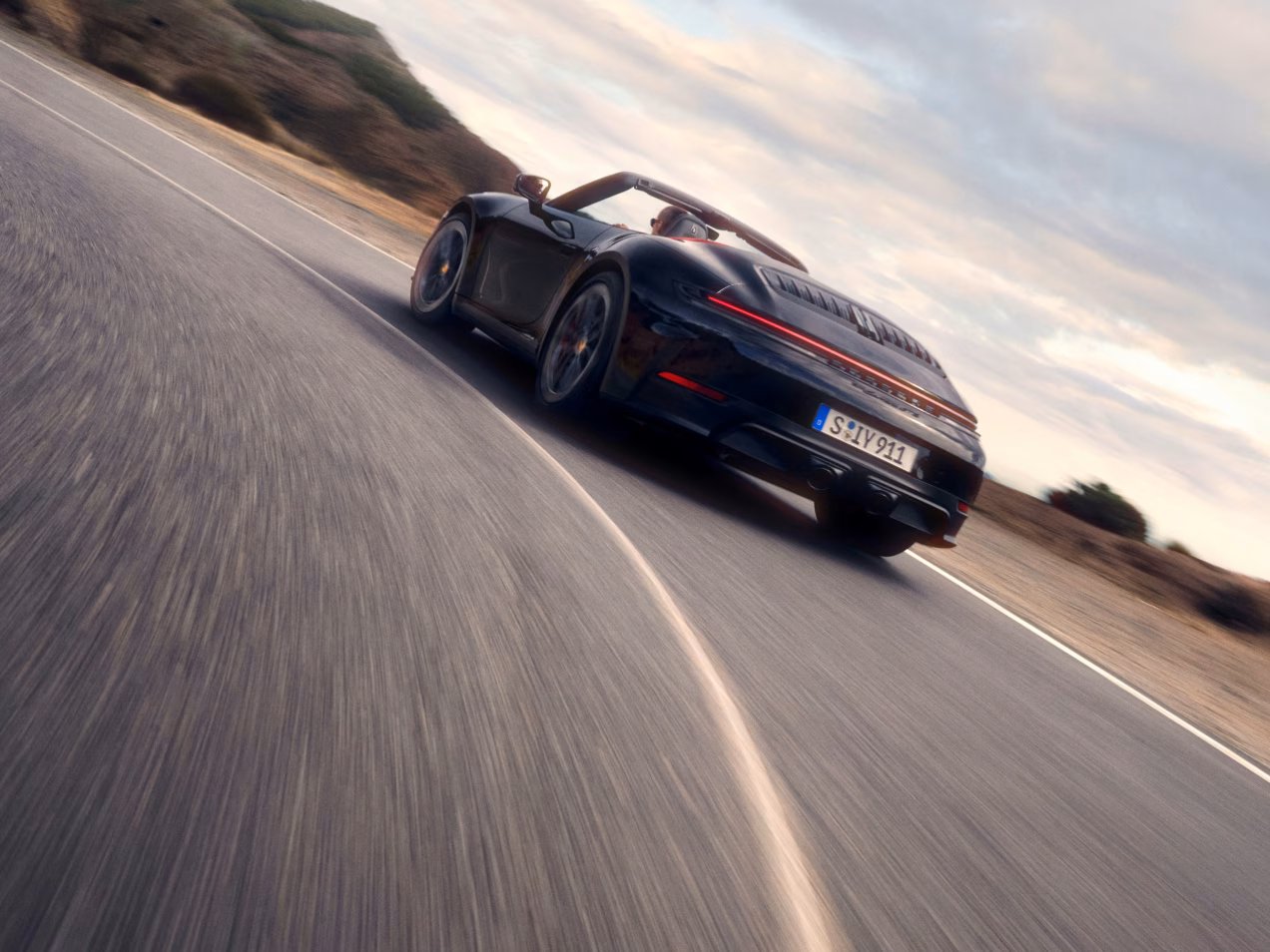 Porsche 911 Carrera GTS Cabriolet in Schwarz fährt auf Straße um Kurve. Blick von hinten aufs Heck.