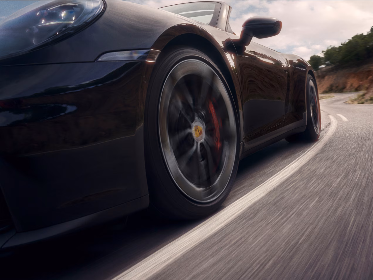 Porsche 911 Carrera GTS Cabriolet in Schwarz fährt auf Straße. Blick von vore auf die Seite.
