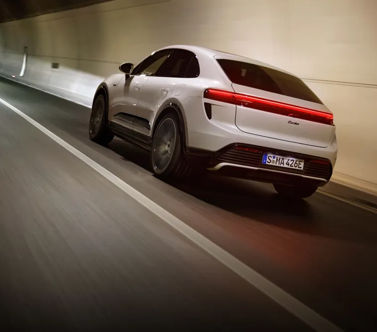 Porsche Macan Turbo in Ice Grey Metallic driving along a city street. Rear and side visible.