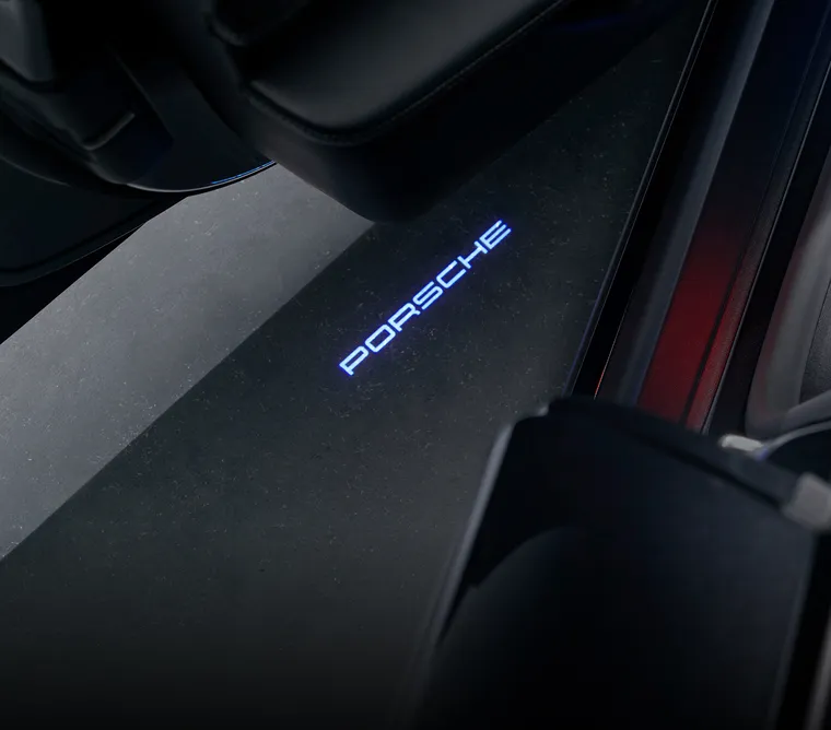 Die LED-Türprojektoren des Porsche Taycan 4S Black Edition projizieren bei geöffneten Türen den weiß leuchtenden „PORSCHE“ Schriftzug auf den Boden.
