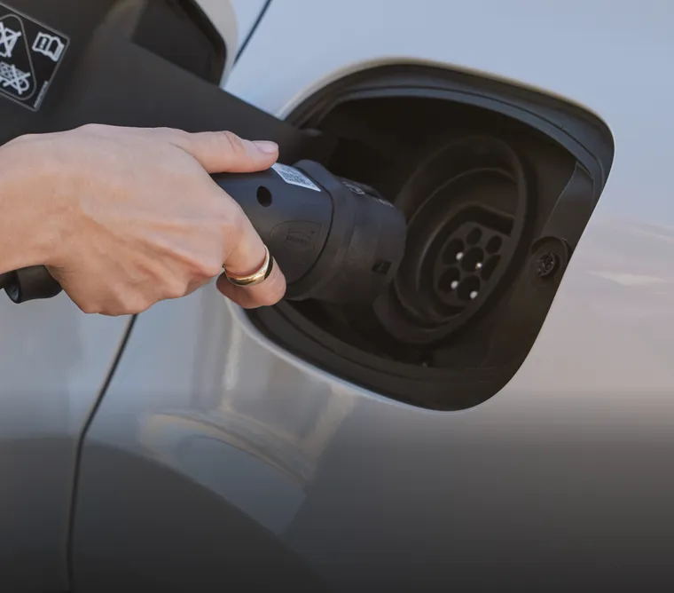 Detailed view: a person inserting the charging plug into the charging socket of a Porsche Cayenne E-Hybrid model in Carrara White Metallic.