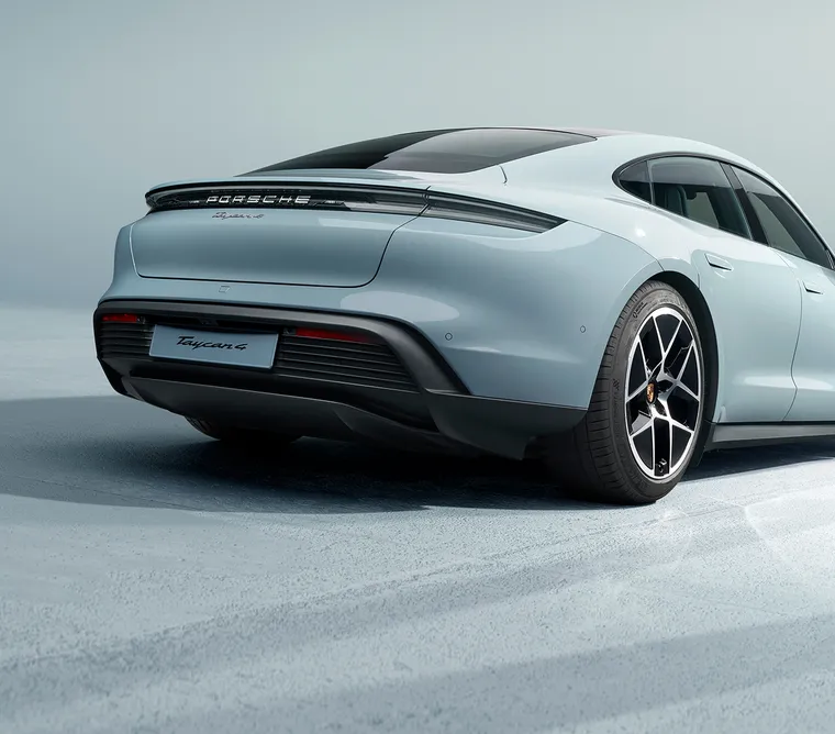 Porsche Taycan Turbo S in Ice Grey Metallic in front of a dark background. Rear and side view from behind.
