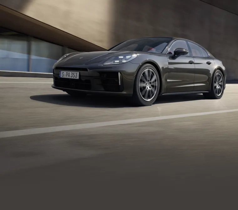 Porsche Panamera 4 in vulkaangrijs metallic rijdt langs een gebouw. Zicht op het front en de zijkant.