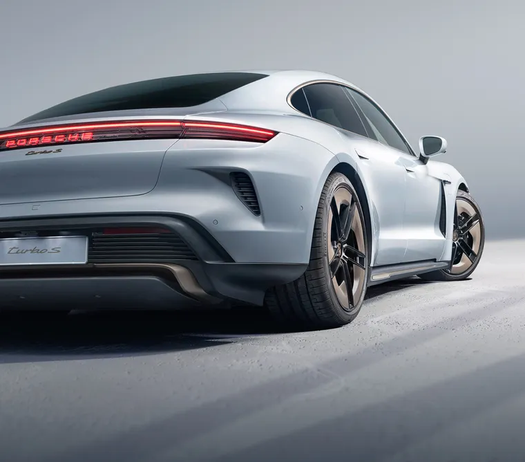 Porsche Taycan Turbo S in Eisgraumetallic vor dunklem Hintergrund. Blick von hinten auf Heck und Seite.