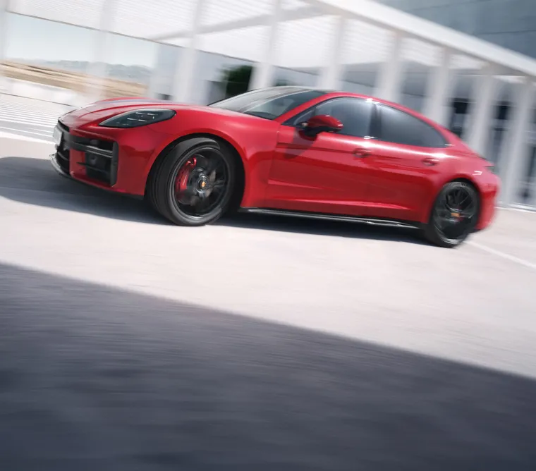 Porsche Panamera GTS in Carmine Red driving through the city. Rear and side view from behind.