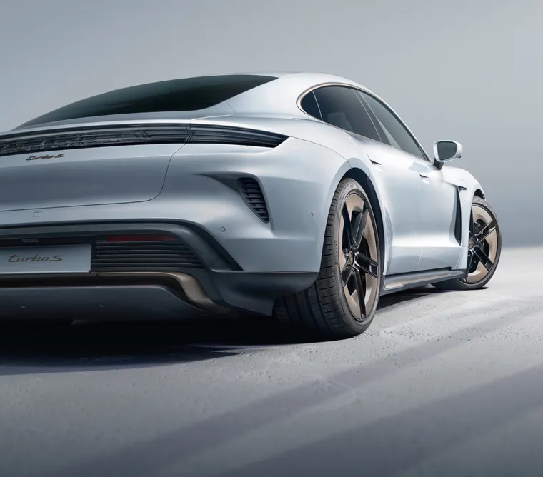 Porsche Taycan Turbo S in Ice Grey Metallic in front of a dark background. Rear and side view from behind.