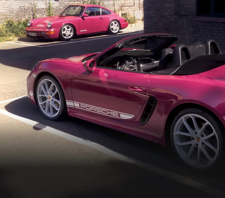 Porsche 718 Boxster Style Edition in Ruby Star Neo with White Contrast Package parked in front of 911 Carrera RS 3.6 (964). Side visible.