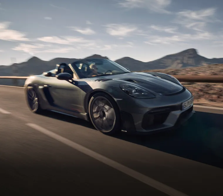 El Porsche 718 Spyder RS en color Gris Vanadium Metalizado circulando por la carretera. Vista de la parte delantera y el lateral.