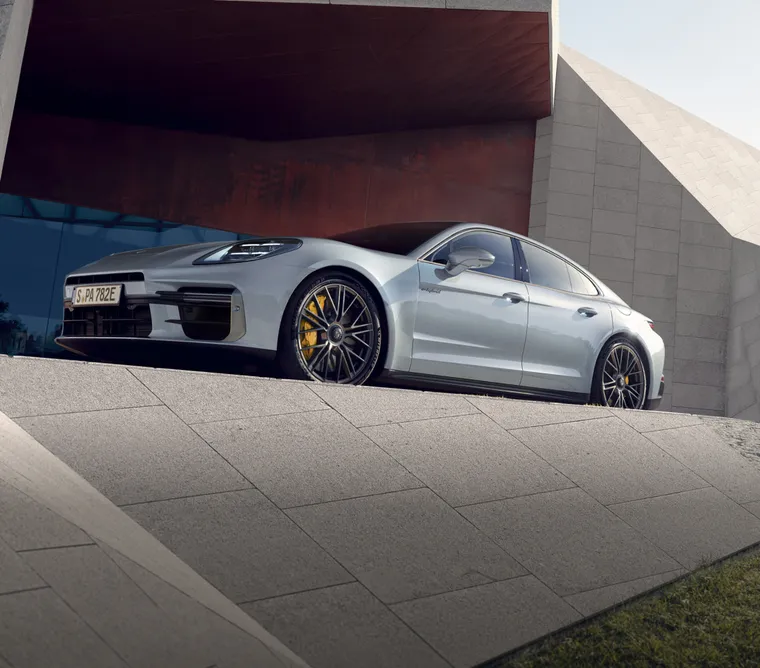 Porsche Panamera Turbo S E-Hybrid i Ice Grey Metallic står framför en byggnad. Vy framifrån av fronten.