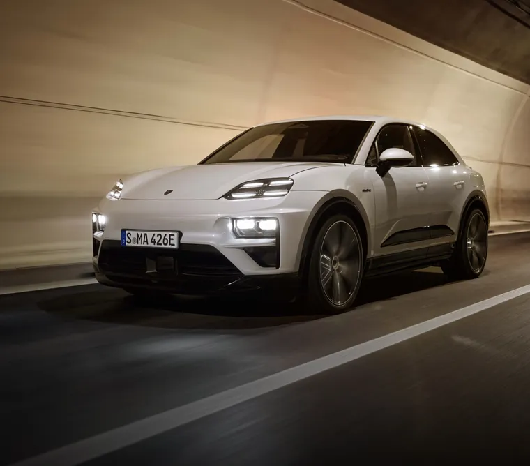 Porsche Macan Turbo in Eisgraumetallic fährt auf Straße in Vorstadt. Heck und Seite sichtbar.