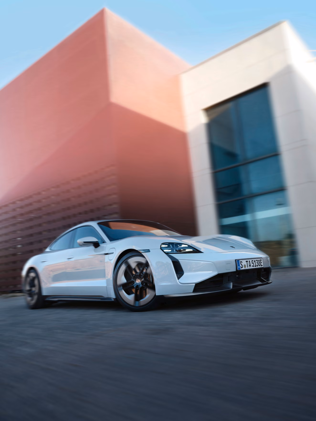 Porsche Taycan Turbo S in Ice Grey Metallic driving along a city street. Front and side views.