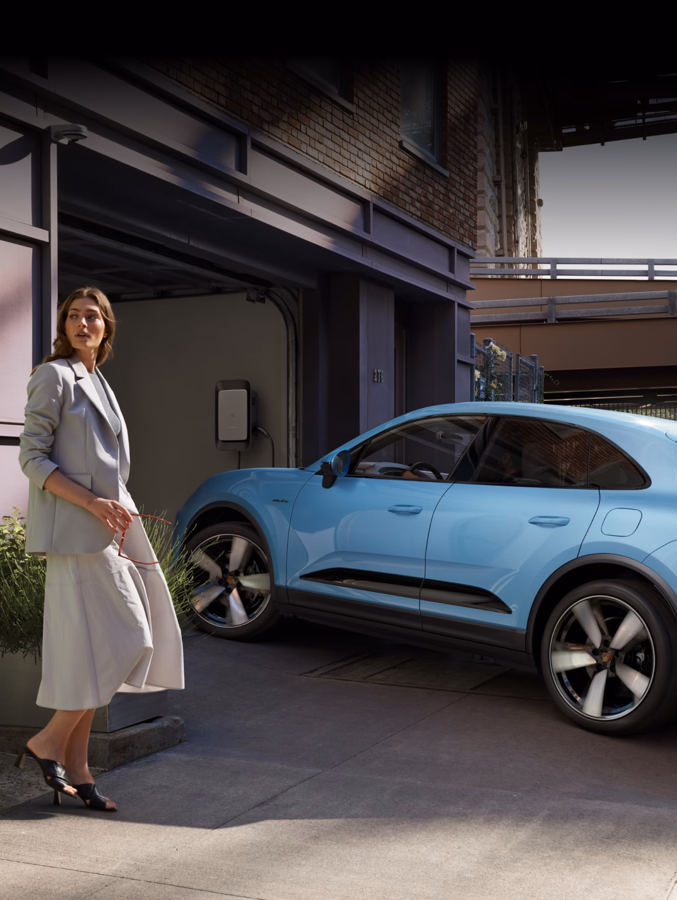 Porsche Macan in Frozen Blue Metallic charging at a wallbox. Side and front visible.