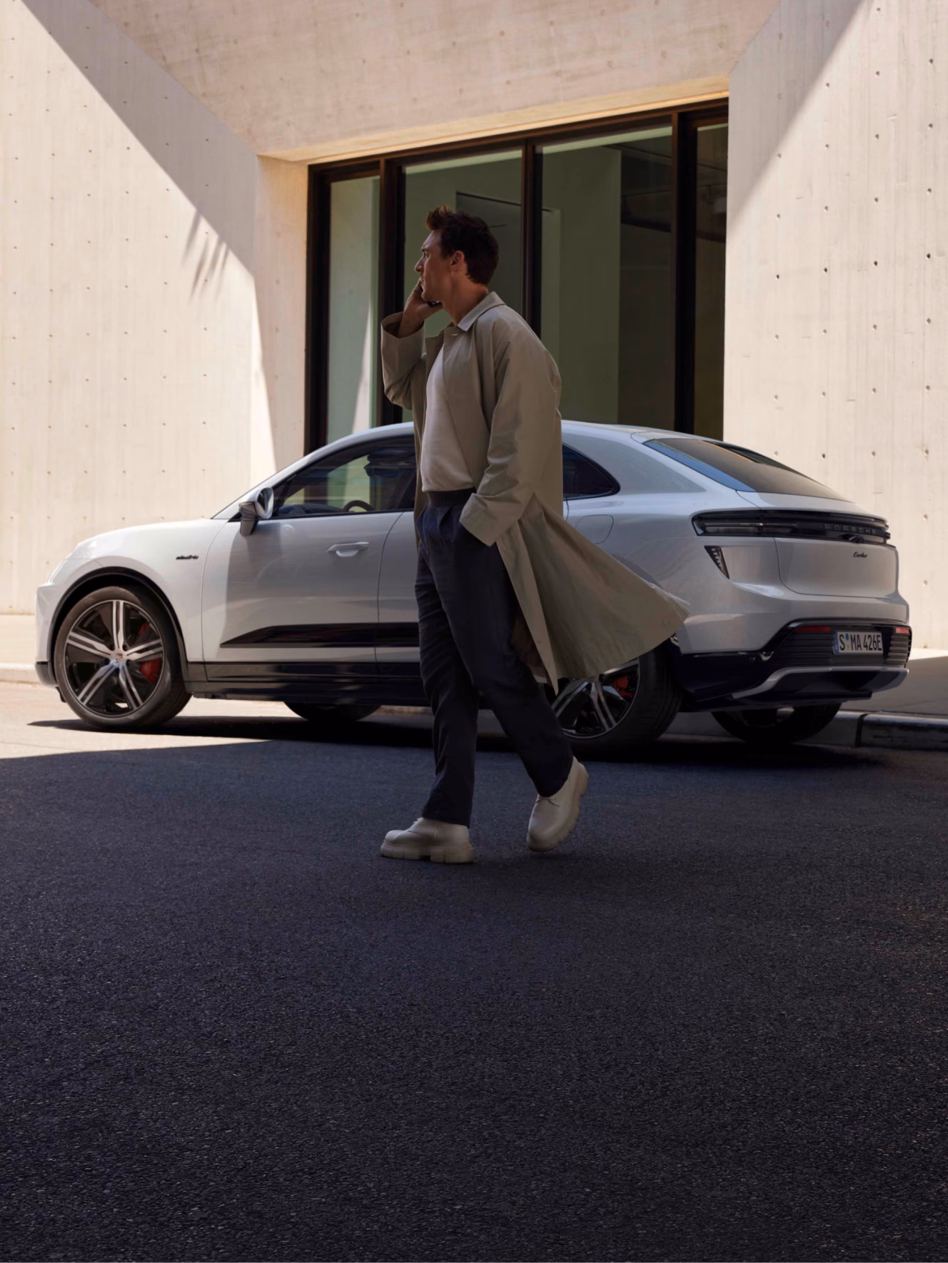Man on phone in front of Porsche Macan Turbo in Ice Grey Metallic in rear/side view.