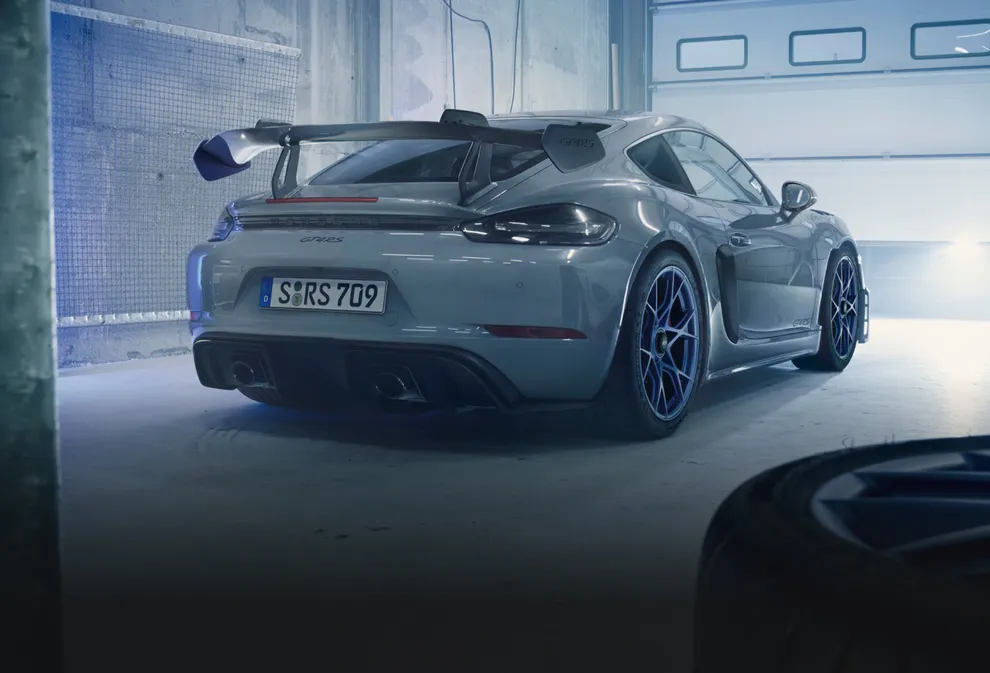 Porsche 718 Cayman GT4 RS in Arctic Grey with Weissach Package in a garage. View of the rear with rear wing in carbon-weave finish.