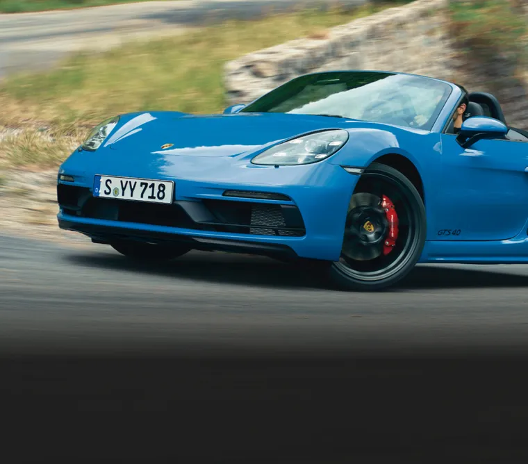 O Porsche 718 Boxster GTS 4.0 dirigindo em uma curva fechada de uma estrada sinuosa. Visão da frente com a seção dianteira específica do GTS 4.0.