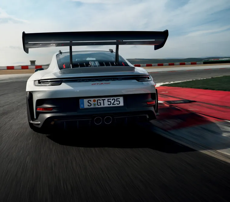The Porsche 911 GT3 RS in Ice Grey Metallic taking a corner on a race track. View of rear end from behind.