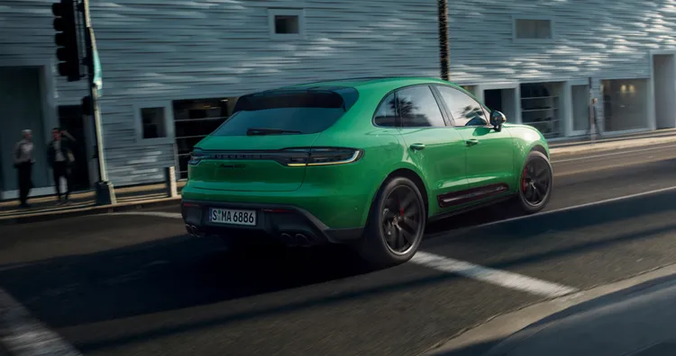 市街地を走り抜けるパイソングリーンのMacan GTS。リアビューとサイドビュー