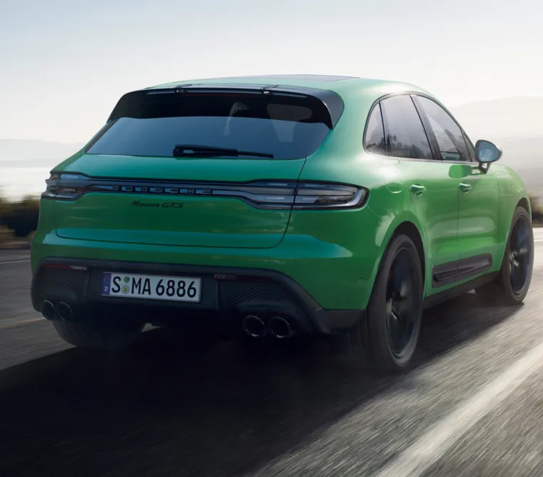 Un Porsche Macan GTS en color Verde Python circulando por un camino rural. Vista de la parte trasera desde detrás.
