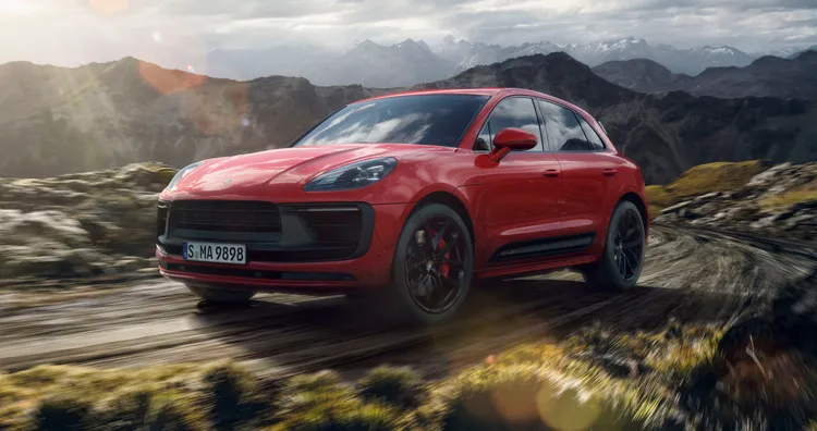 Un Porsche Macan GTS en color Rojo Carmín circulando por un paisaje de montaña. Vista frontal y lateral.