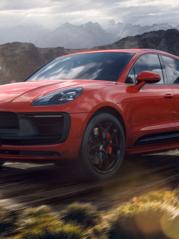 Porsche Macan GTS in Carmine Red driving on a gravel road. Front and side views.