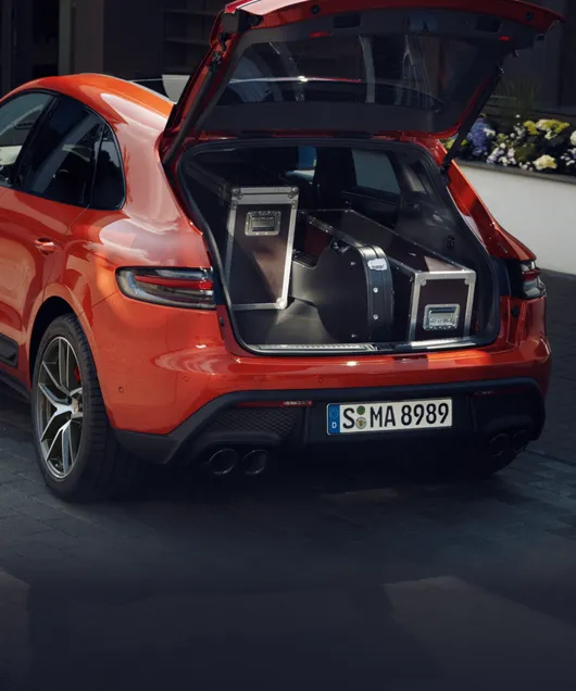 Porsche Macan S em Papaia metálico em uma entrada de garagem. Vista do compartimento de bagagem aberto cheio de malas.