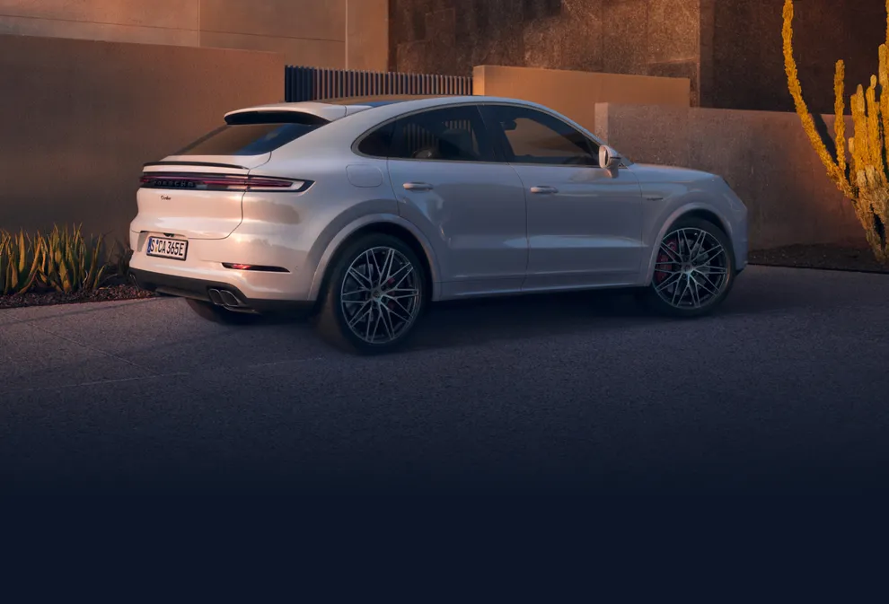 Porsche Cayenne Turbo E-Hybrid Coupé in Carraraweißmetallic in städtischem Umfeld. Blick auf Heck und Seite.