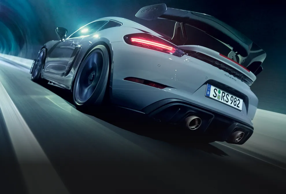 Porsche 718 Cayman GT4 RS en color Gris Arctic con paquete Weissach atravesando un túnel. Vista de la parte trasera y el lateral.