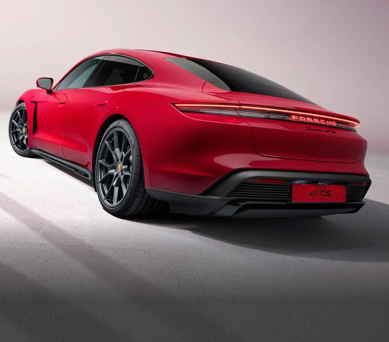 Porsche Taycan Turbo S in Ice Grey Metallic in front of a dark background. Rear and side view from behind.