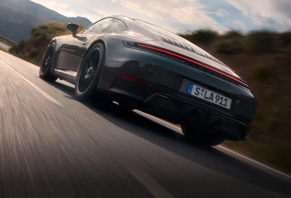Un Porsche 911 Carrera GTS en color Gris Pizarra Neo circulando por una carretera. Vista de la parte trasera y el lateral.