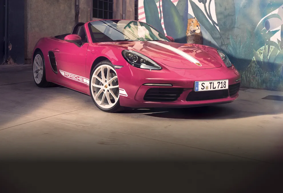 Porsche 718 Boxster Style Edition en Ruby Star Neo avec pack de contraste en Blanc devant une peinture murale. Vue de face et latérale.