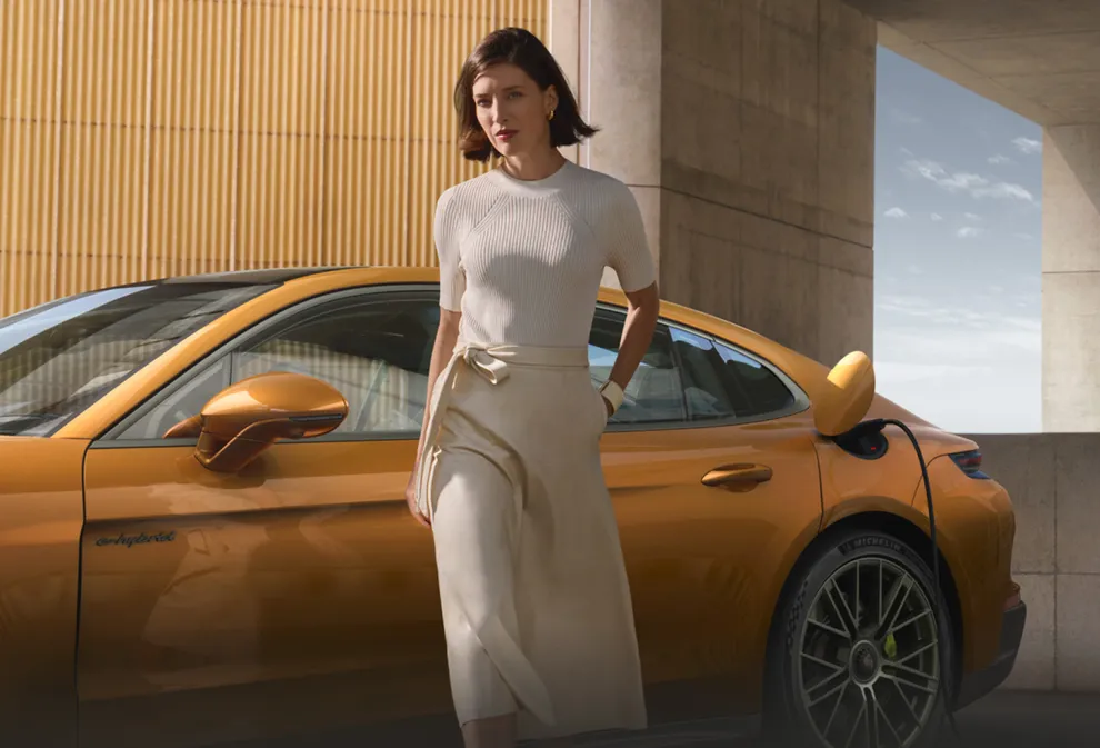 Porsche Panamera Turbo E-Hybrid in Madeira Gold Metallic being charged. Side view. A woman in the foreground moves away from the vehicle.