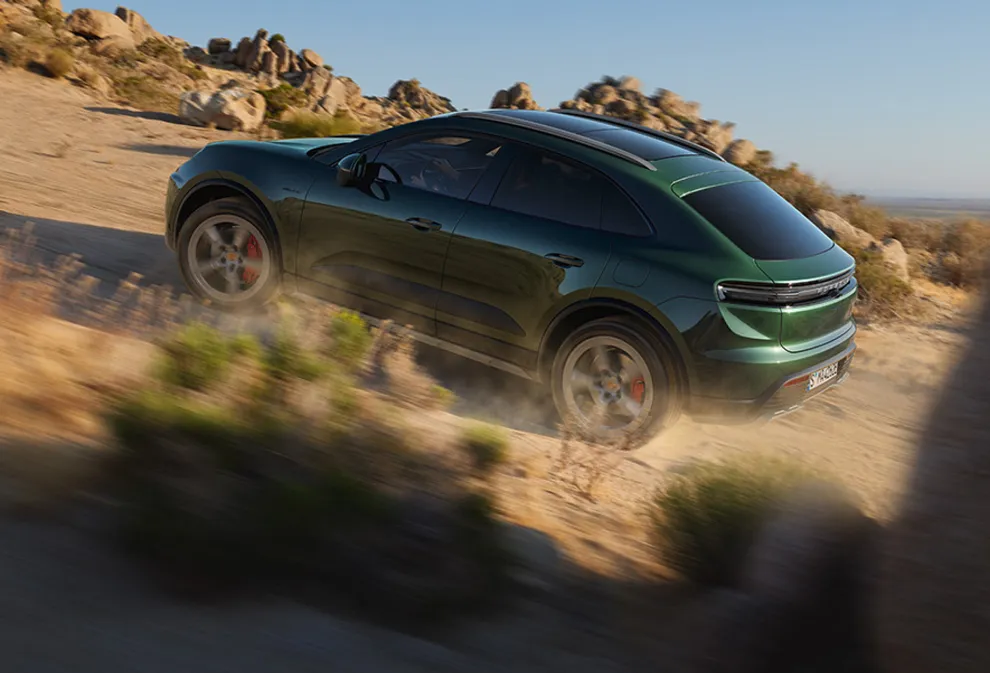 Porsche Macan 4S in Oakgrünmetallic fährt Steigung hinauf. Heck und Seite sichtbar.