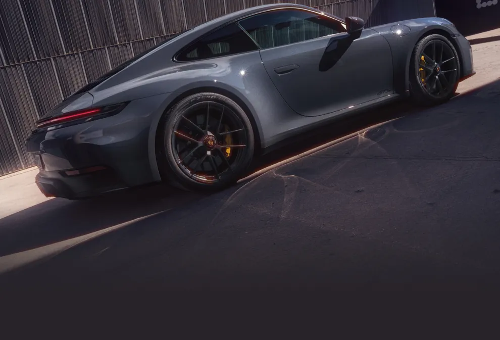 Porsche 911 Carrera GTS in Schiefergrau neo steht vor dunkelgrauer Wand. Blick auf die Seite.