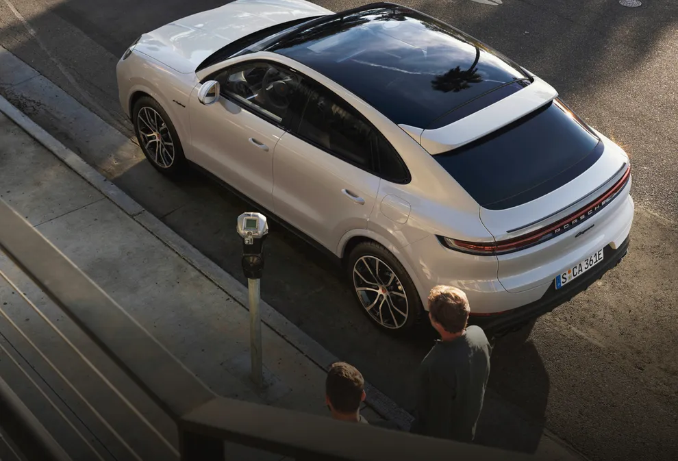 Porsche Cayenne E-Hybrid Coupé цвета белый металлик (Carrara White Metallic). Вид сверху на заднюю и боковую часть автомобиля и на панорамную стеклянную крышу.