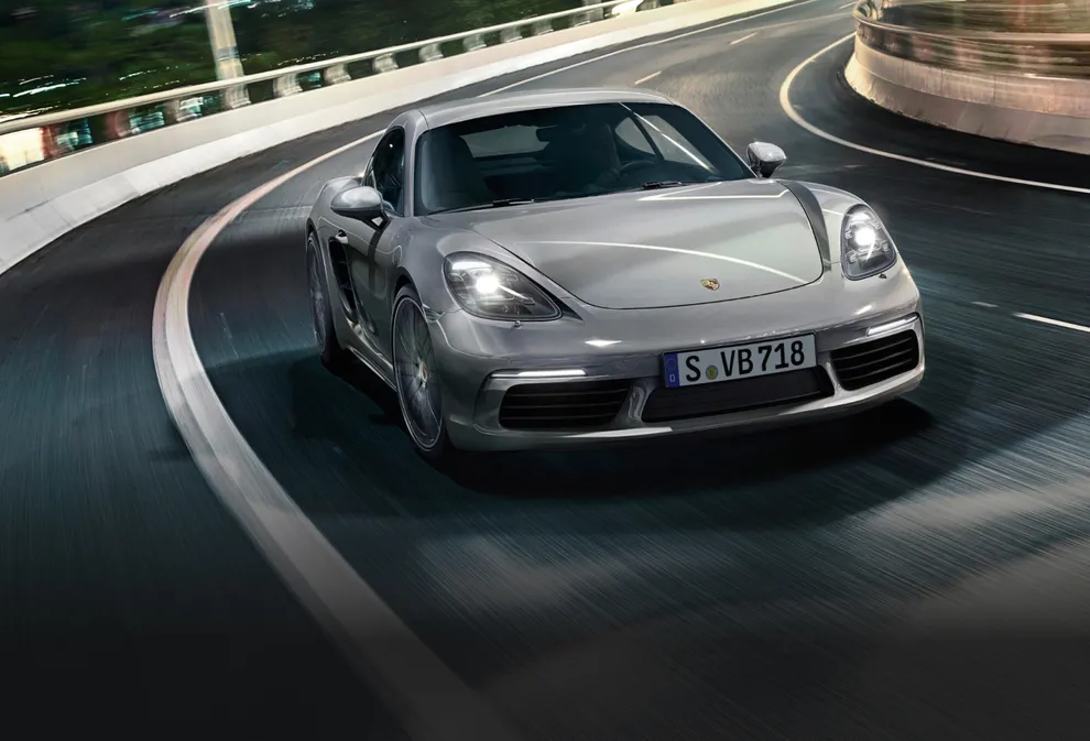 Porsche 718 Cayman S en color Plata GT Metalizado circulando por una carretera. Vista de la parte delantera.