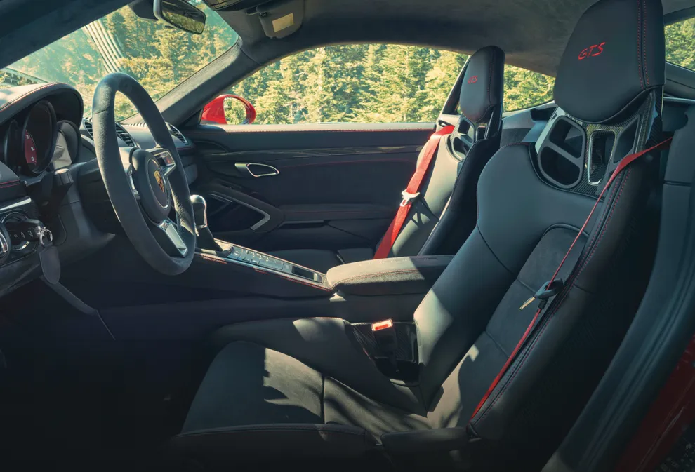 Interior del Porsche 718 Cayman GTS 4.0: vista del puesto de conducción con asientos deportivos a través de la puerta abierta del conductor.