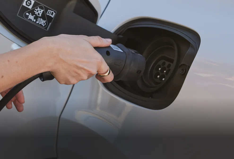 Detailed view: a person inserting the charging plug into the charging socket of a Porsche Cayenne E-Hybrid model in Carrara White Metallic.