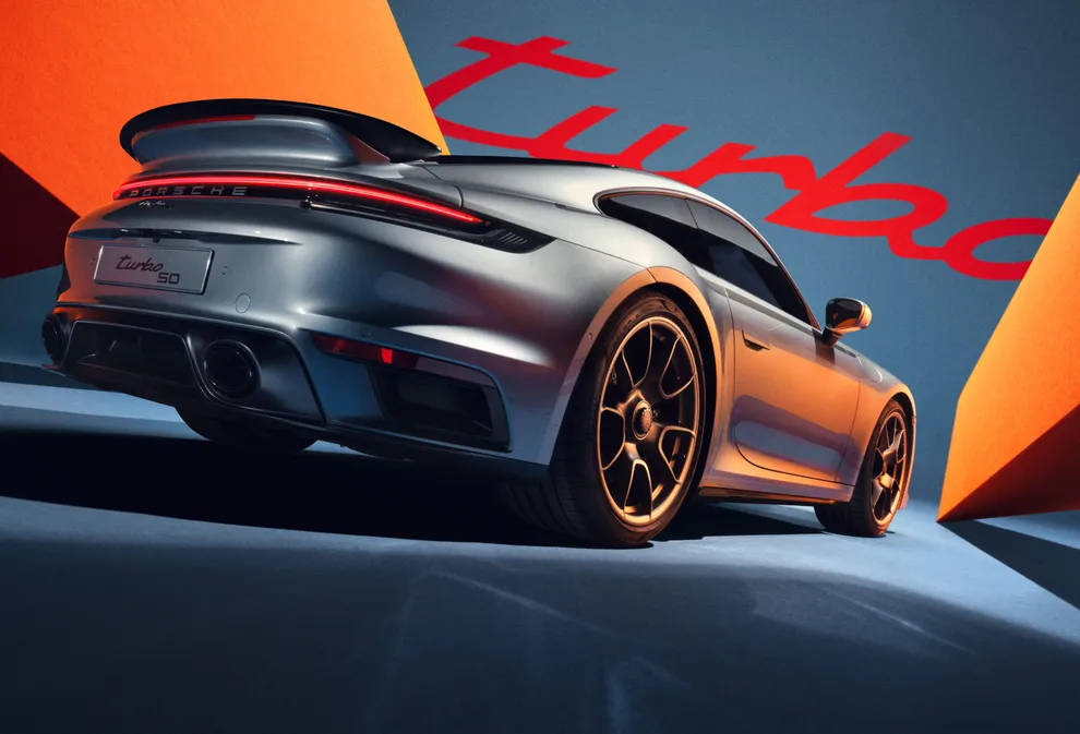 De Porsche 911 Turbo 50 Years Edition in GT-zilver metallic is van de achterkant te zien tegen een blauw-oranje achtergrond. 