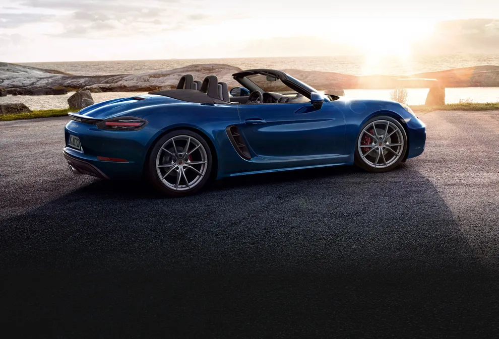 Visão lateral de um Porsche 718 Boxster S em Azul Genciana Metálico em uma paisagem ao pôr do sol.